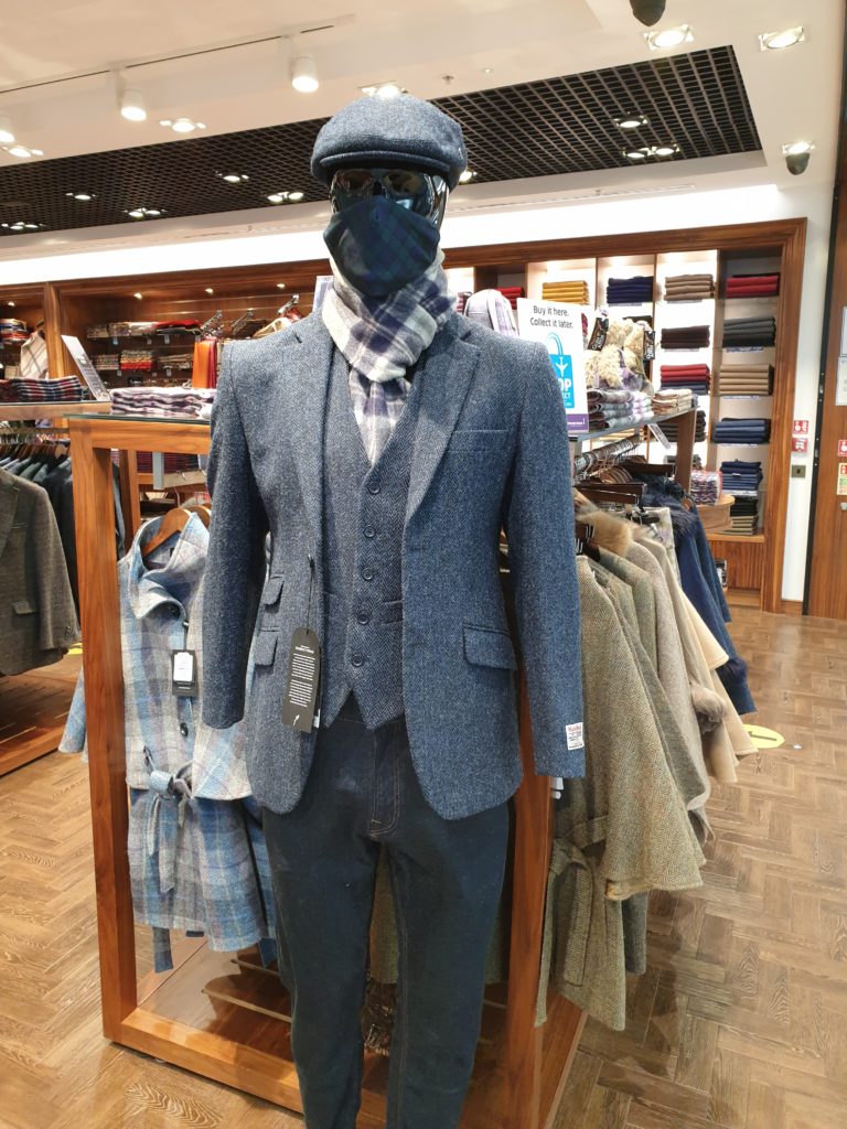 A mannequin in an airport shop wears smart clothes and a mask.